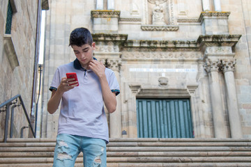 young teenage man with mobile phone walking in the city