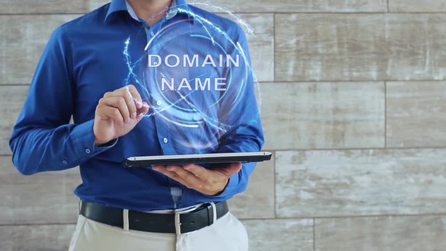 Man activates a conceptual hologram with text Domain name. The guy in the blue shirt and light trousers with a holographic screen gadget on the background of the wall