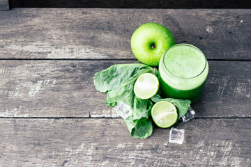 Green apple smoothie in glass and kale leaves on wooden table