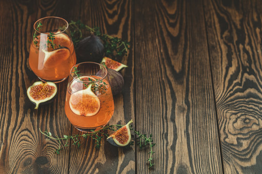 Pink cocktail with fig, thyme and ice in glass on dark wooden background, close up