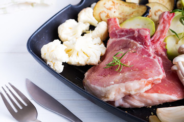 Raw lamb ribs marinating with fresh vegetables in a grill pan on a white background,