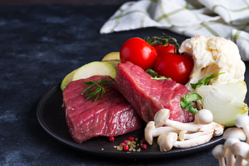 Raw beef steak on the bone with fresh vegetables in a grill pan on a concrete background, top view