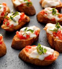 Crostini, toasts, grilled baguette slices with tomatoes, mozzarella cheese and fresh basil on a black background, close-up.   Delicious appetizer or breakfast