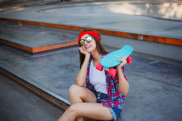 Portrait of stylish skater woman in skatepark. Attractive girl in red plaid shirt, mirrored sunglasses, shorts rests with a skate © splitov27