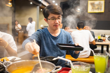 Man holding bamboo chopsticks boiling a piece of sliced meat in Japanese Shabu restaurant