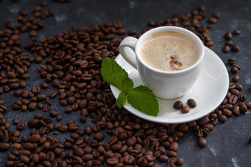 A cup of delicious, aromatic coffee. It is on a substrate of coffee beans. Has a lush, white foam. Decorated with mint leaves. 