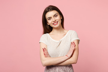 Attractive smiling young woman in casual light clothes posing isolated on pastel pink background, studio portrait. People lifestyle concept. Mock up copy space. Holding hands crossed, looking camera.