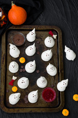 Ghosts Halloween Meringues with chocolate and berry sauces on an old baking sheet on a black background.  Food idea for halloween party.