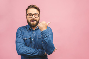 Surprised happy bearded man in shirt pointing away isolated over pink background.