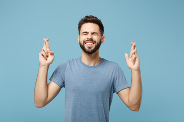 Young funny man in casual clothes posing isolated on blue wall background. People lifestyle concept. Mock up copy space. Waiting for special moment, keeping fingers crossed, eyes closed, making wish.