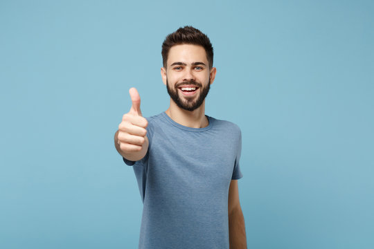 Young smiling cheerful handsome man in casual clothes posing isolated on blue wall background, studio portrait. People sincere emotions lifestyle concept. Mock up copy space. Showing thumb up.