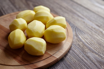 Potatoes on wooden chopping board on brown table. Cooking food from natural products. Root vegetable. Raw ingredient: uncooked whole peeled potatoes