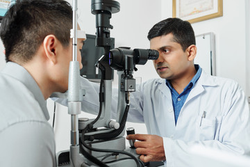 Indian serious optometrist working with his patient he using special medical equipment and examining the eyesight at hospital