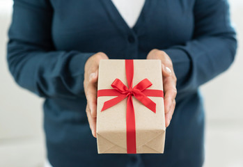 Senior woman in blue sweater is holding a brown gift box