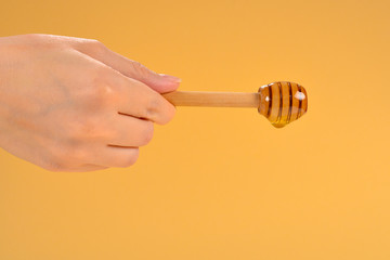 Dipper with honey in woman hand on orange background. Space for text or design.