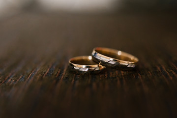 elegant wedding engagement rings in white and yellow gold on brown chocolate wooden background, close-up, copy space