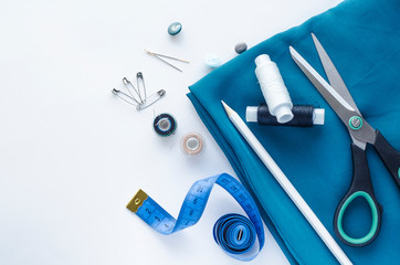 Desktop Accessories for sewing on a white background. Roll of blue satin fabric, tape measure, scissors, needles. Fashion, Design studio for tailoring, atelier concept.  Flat lay, top view, copy space