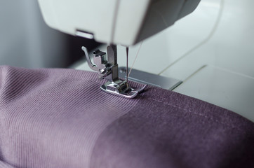Sewing machine with a needle  sews purple fabric and thread, closeup. sewing process. studio atelier equipment