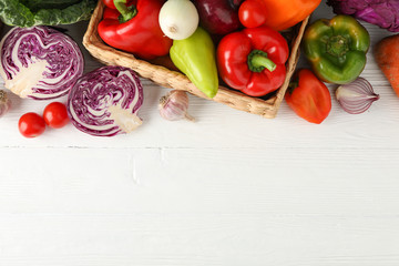 Fototapeta na wymiar Wicker basket and vegetables on white wooden background, top viewWicker basket and vegetables on white wooden background, top view