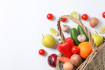 Wicker basket, vegetables and fruits on white background, space for text