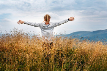 A young girl in the mountains is resting, looking at the sky and stretching her arms up. The girl feels free in the mountains like a bird, she thanks God for her life