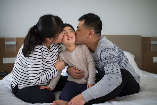 Parents kiss little boy in bedroom