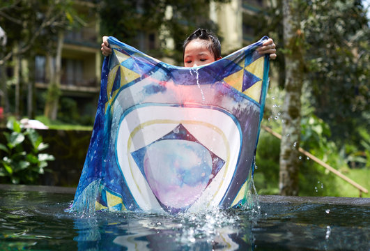 Cute Asian girl playing in an infinity pool with mandala scarves in the woods of nature
