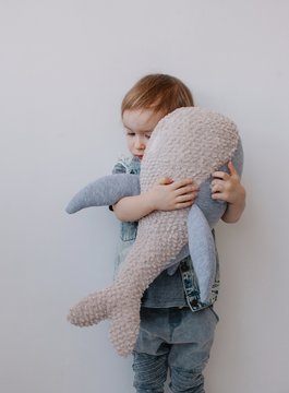 Lovely boy hugging his whale plush toy by the white wall