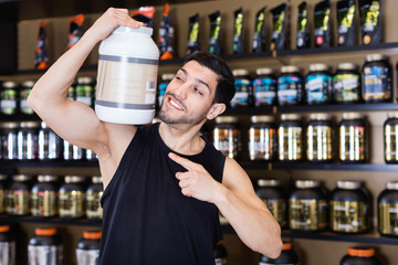 Attractive athletic man on shoulder  sport food products in store, showing his power