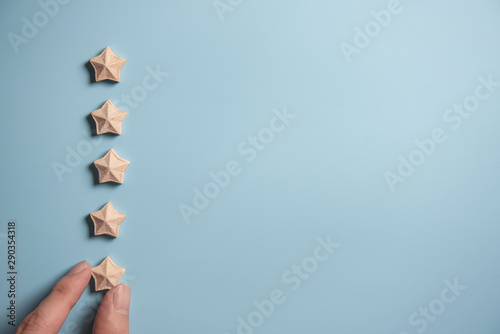 Man Hand putting wooden five star shape on blue background. Best Excellent Services Rating for Satisfaction.