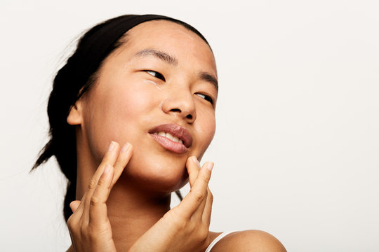 Young natural asian woman portrait applying moisturiser.
