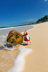 Greeting card with Santa toy and coconut on beach close to sea