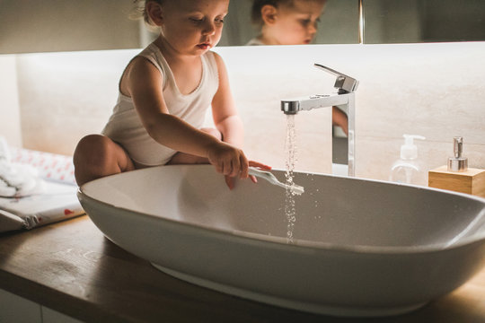 Baby washing the toothbrush in a sink sitting on a counter in a bathroom
