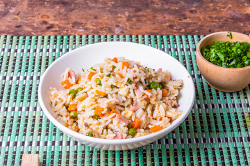 Cantonese rice - a traditional Chinese dish of fried rice, eggs, ham, peas, carrots and spices in a bowl on a bamboo napkin, chopsticks, close-up