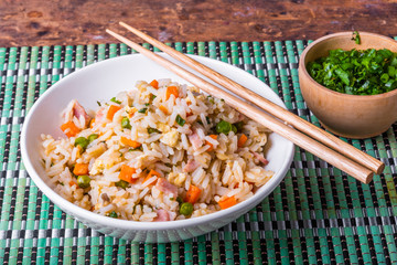 Cantonese rice - a traditional Chinese dish of fried rice, eggs, ham, peas, carrots and spices in a bowl on a bamboo napkin, chopsticks, close-up