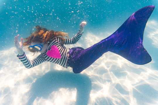 Girl on family vacation exploring diving in cool blue swimming pool mermaid tail