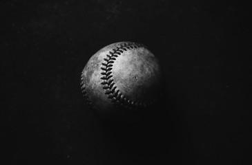 Low key baseball closeup in shadows with black background.  Dark and moody sports image.