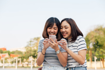2 Asian girlfriends using mobile phone together outdoor