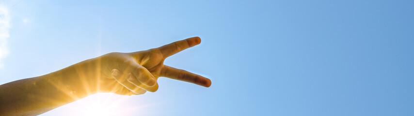 Kinderhand Victory-Zeichen / peace - Hintergrund blauer Himmel mit Sonne