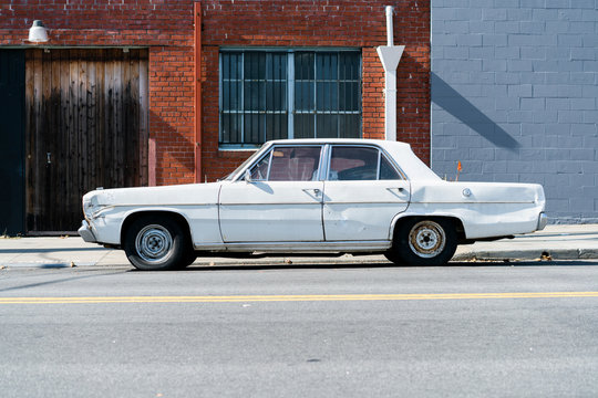 An old beat up white car parked in an urban factory zone