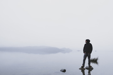 Junger Wanderer steht auf Felsen in einem See bei Nebel 