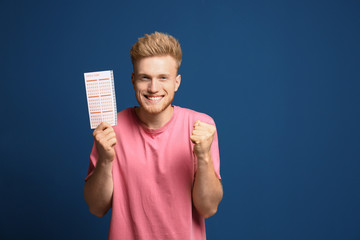 Portrait of happy young man with lottery ticket on blue background - obrazy, fototapety, plakaty