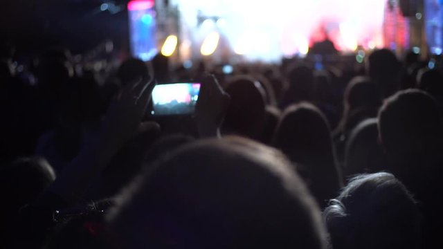 Concert at night, people raise their hands, take pictures on smartphone,