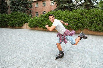 Handsome young man roller skating outdoors. Recreational activity