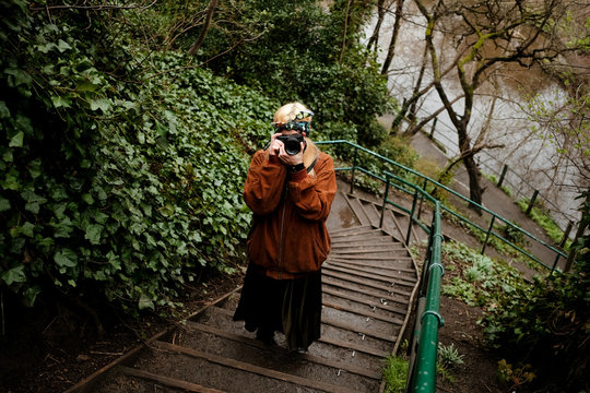 portrait of a blonde woman on a yard close to a river taking photos with her camera