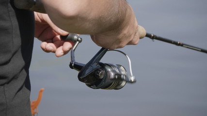 Male hand holding fishing rod and reeling the other hand