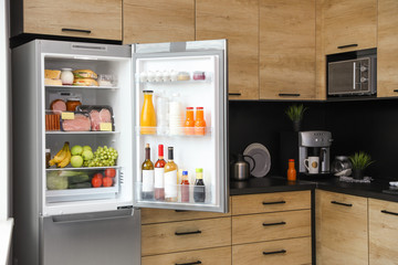 Open refrigerator full of products in kitchen
