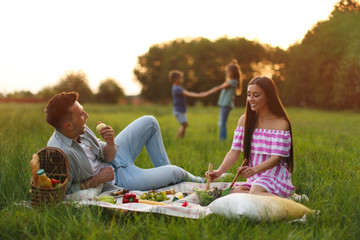 Happy family having picnic in park at sunset