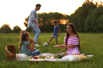 Happy family having picnic in park at sunset