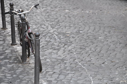 altes Fahrrad lehnt an Begrenzungspfosten auf Platz mit Kopdfsteinpflaster